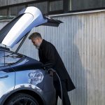 Man charging an EV with a black Easee charger on concrete wall.
